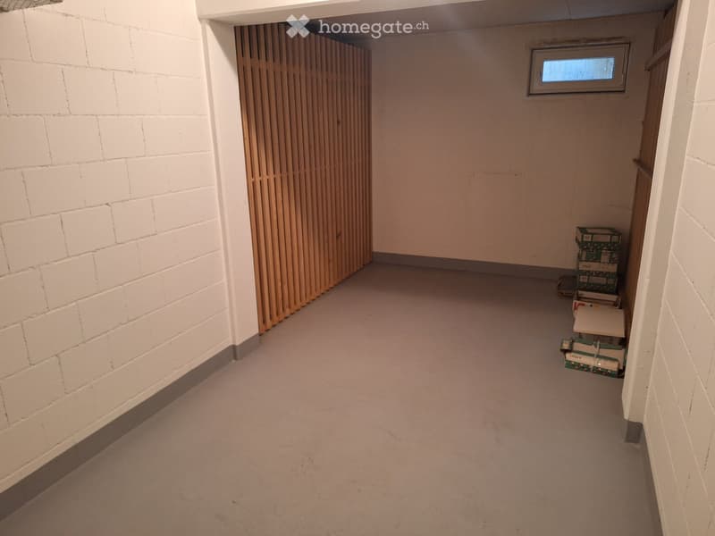Empty hallway with white brick walls, a wooden panel door, and a small window at the far end. Some stacked boxes are visible on the right side.