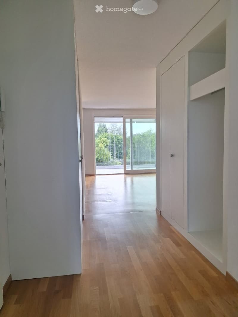 Empty hallway with wooden flooring, white walls, and large glass doors leading to an outdoor area.