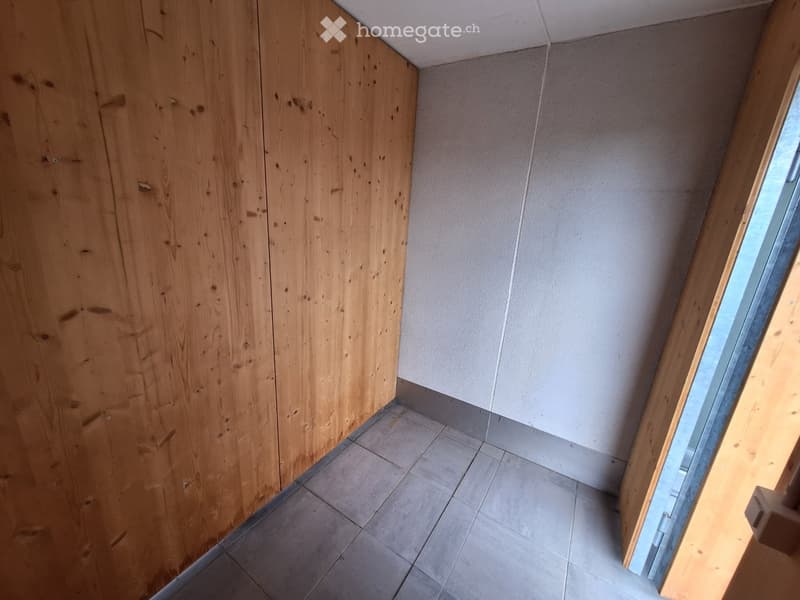 Empty room with wooden walls, tiled floor, and a window allowing natural light to enter.