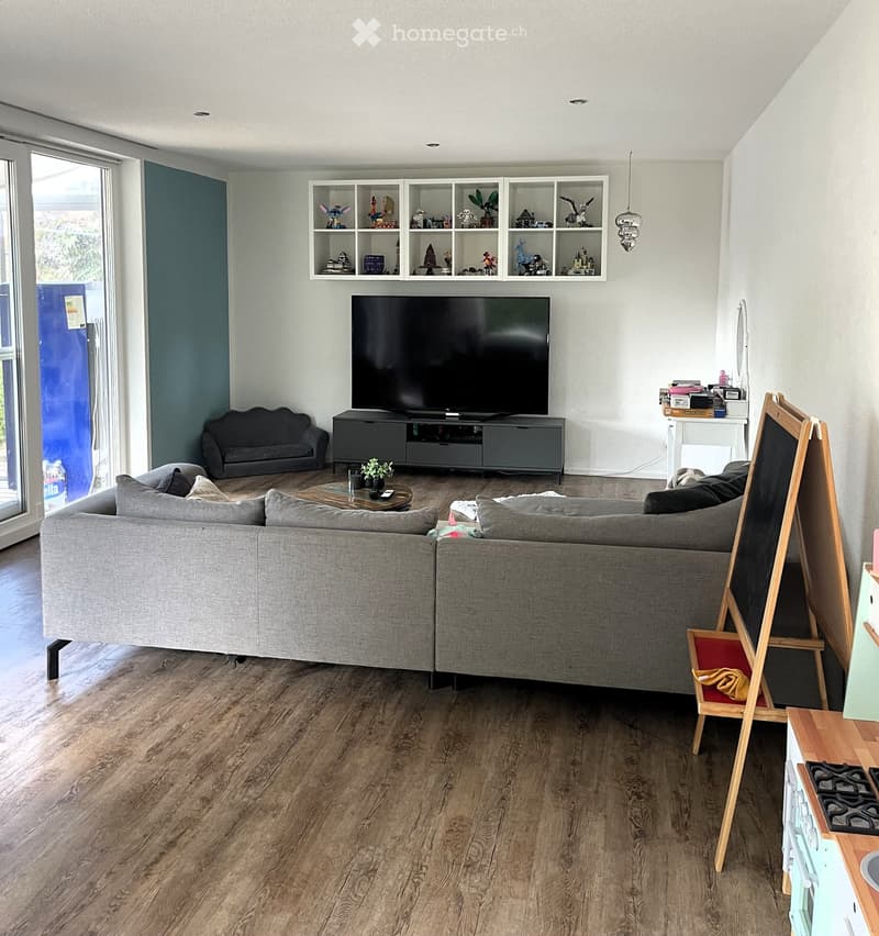 Modern living room with a large sectional sofa, coffee table, TV stand, and shelves with decorative items.