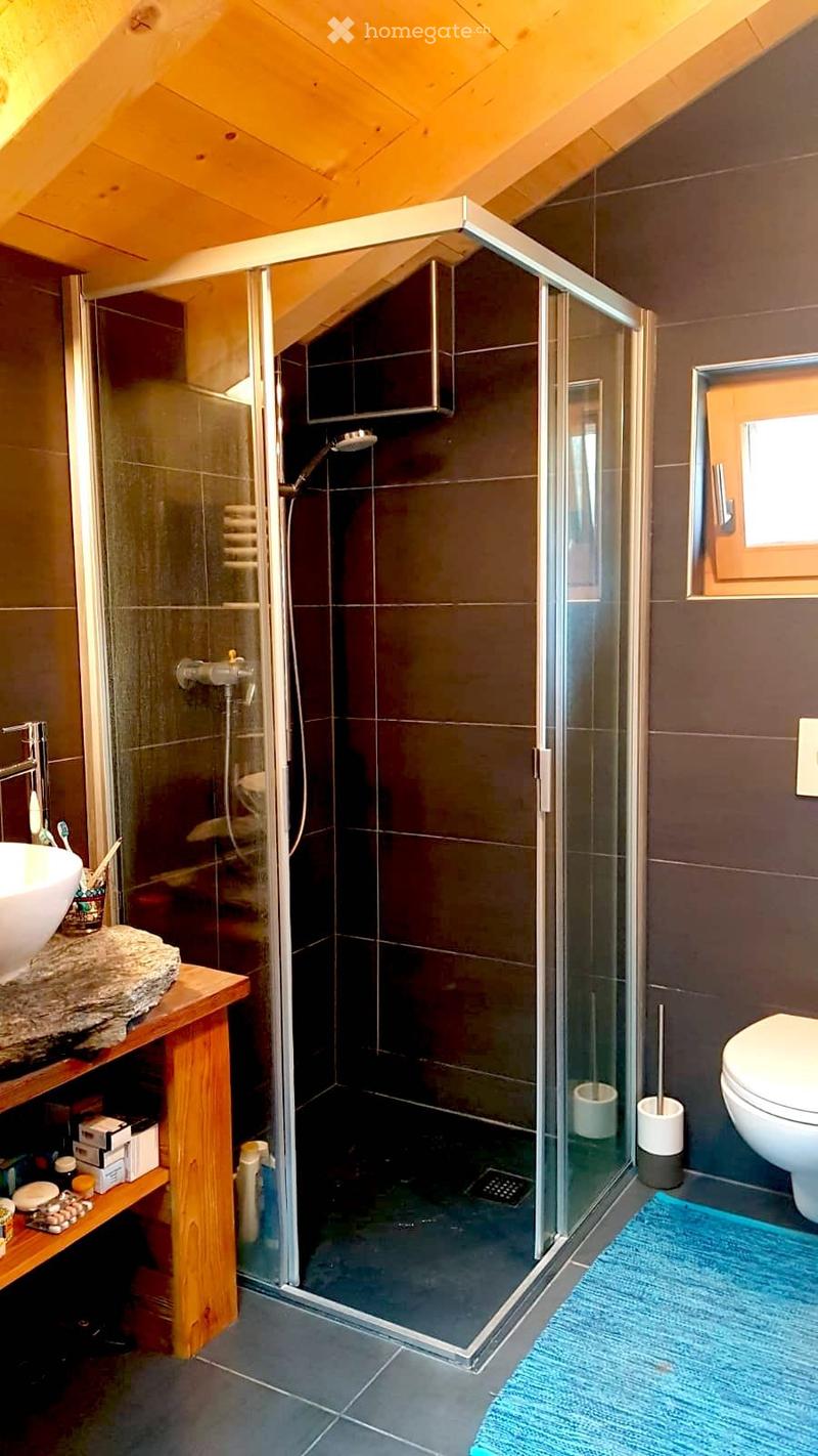 bathroom with a glass shower, white toilet, sink, blue rug, wooden shelf with toiletries, wooden table, wooden ceiling