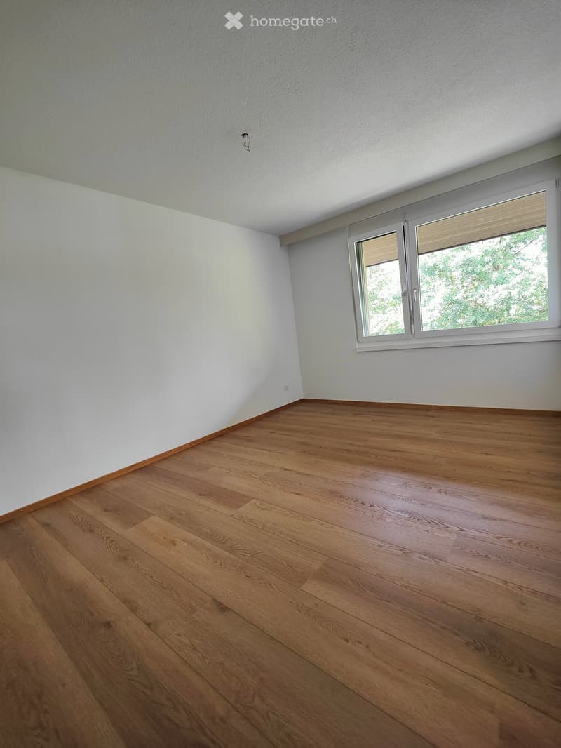 Empty room with light-colored walls and wooden flooring, featuring a large window with blinds.