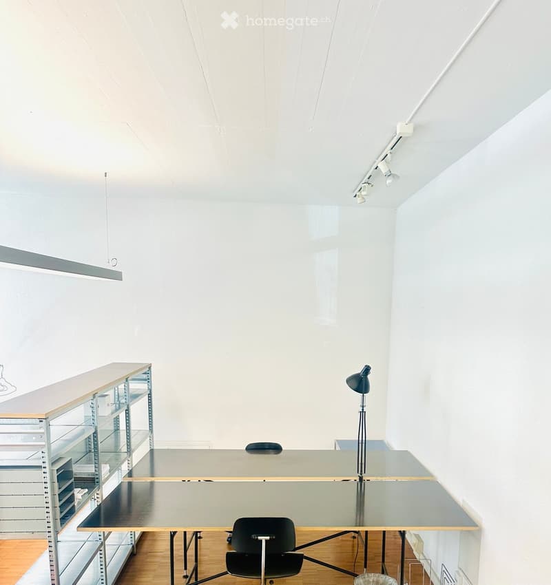 Modern, minimalist room with a large glass table, black chair, metal shelving unit, and track lighting.