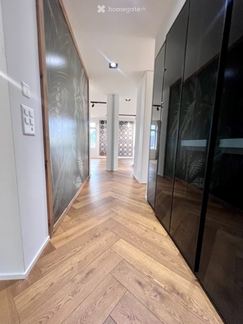 Modern hallway with herringbone wooden flooring, white walls, and built-in dark wood cabinetry on one side.