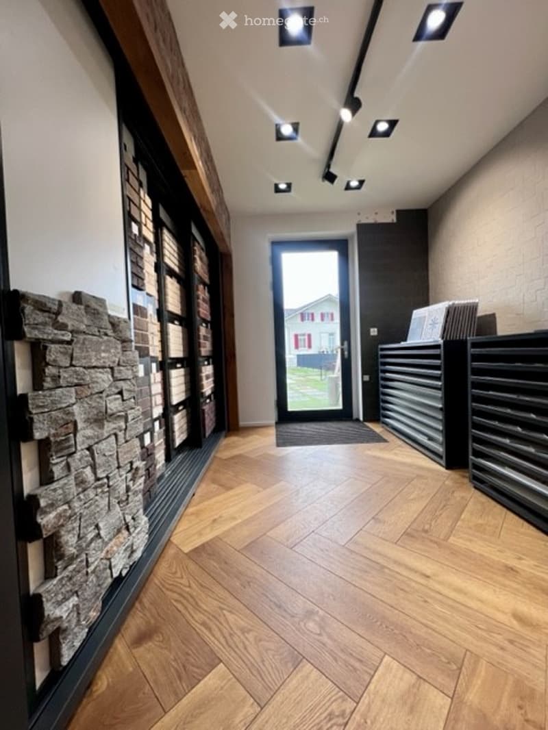 Modern hallway with herringbone wooden flooring, recessed ceiling lights, stone accent wall, and a glass front door leading outside.