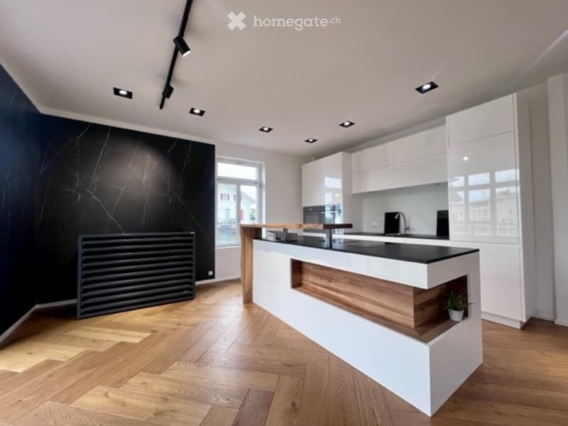 Modern kitchen with white cabinets, black countertops, wooden flooring, and built-in appliances.
