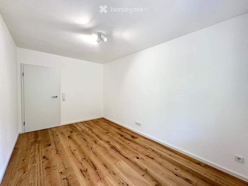 Empty room with light wooden flooring, white walls, and a single door. No furniture or equipment is present.