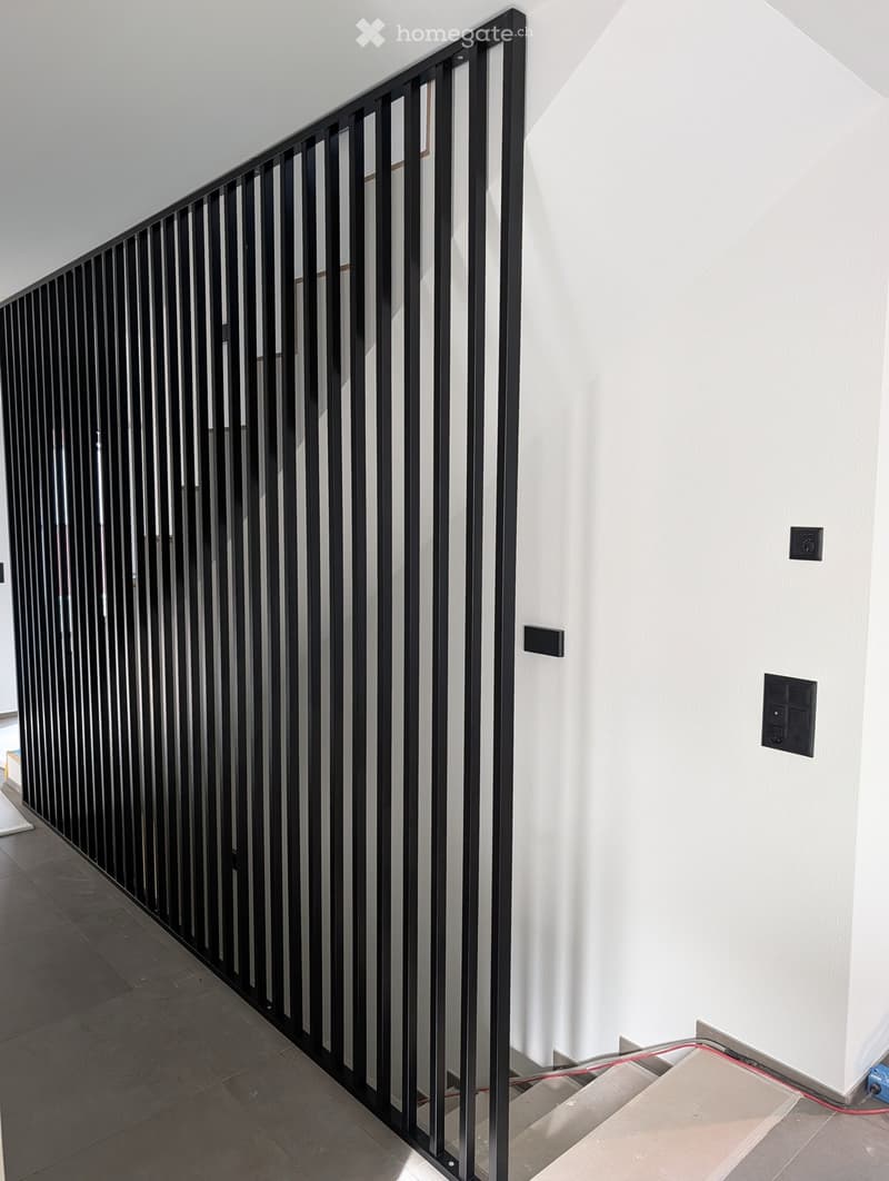 Modern hallway with white walls, dark tiled floor, and a black metal railing leading to an upper level.