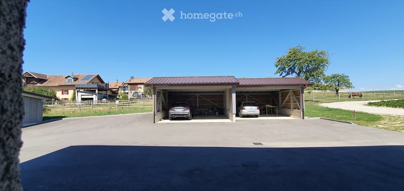 Detached garage with two cars parked inside, located in a rural setting with neighboring houses and a fenced area.