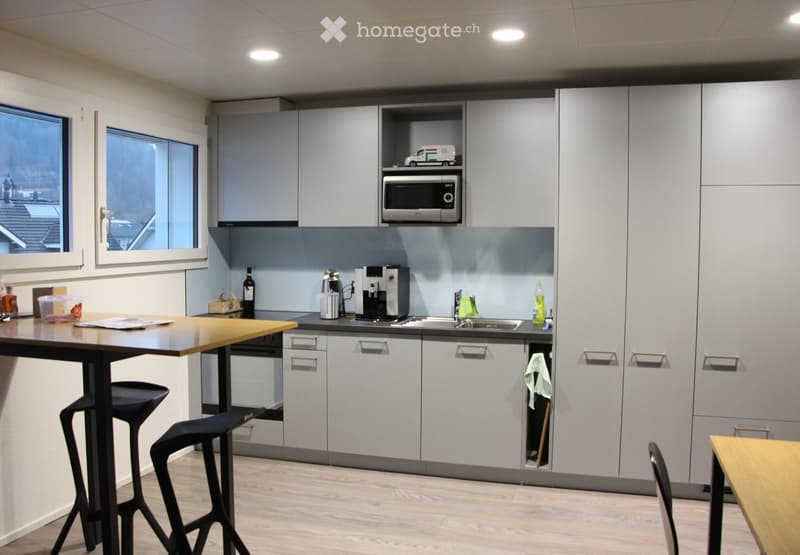 Modern kitchen with grey cabinets, a microwave, coffee maker, sink, and a small dining table with stools.