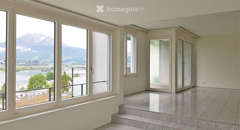 Empty room with large windows offering a scenic mountain and lake view, polished tile floor, and a small step leading to a balcony area.