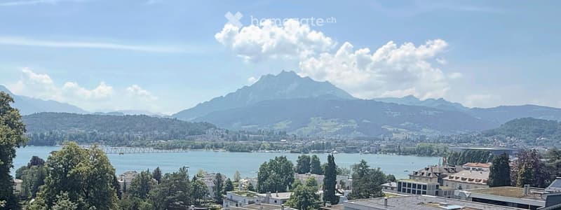 Panoramic view of a cityscape with a lake, mountains, and scattered buildings.