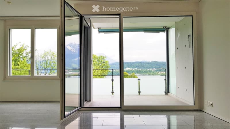 Open hallway with large glass doors leading to a balcony, offering a scenic mountain view and greenery.