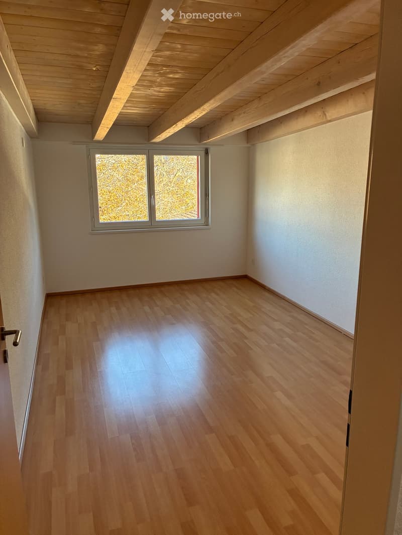 Empty room, hardwood floor, wooden beams, white walls, single window, wall mounted power outlets