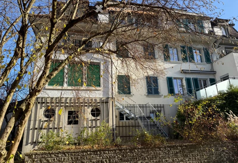 white multi-storey house with green shutters, brick wall, entrance with stairs