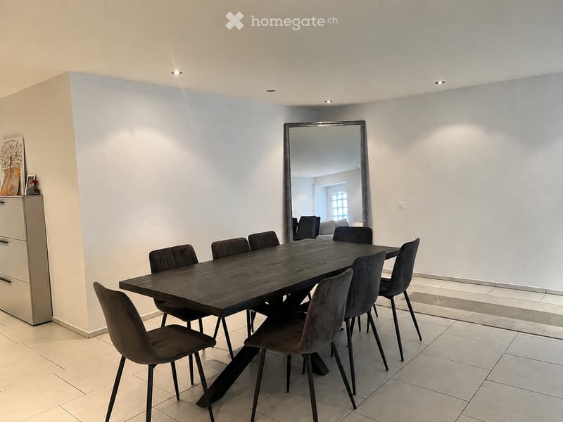 Modern dining room with a dark wooden dining table surrounded by black chairs, a large mirror on the wall, and a sleek cabinet with drawers.