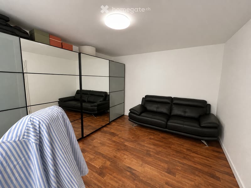 Modern living room with wooden flooring, two black leather sofas, a large mirrored wall, and storage boxes on top of the mirror.