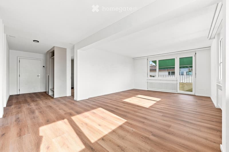 Empty room with white walls, wooden flooring, and large windows with blinds. No furniture or equipment present.