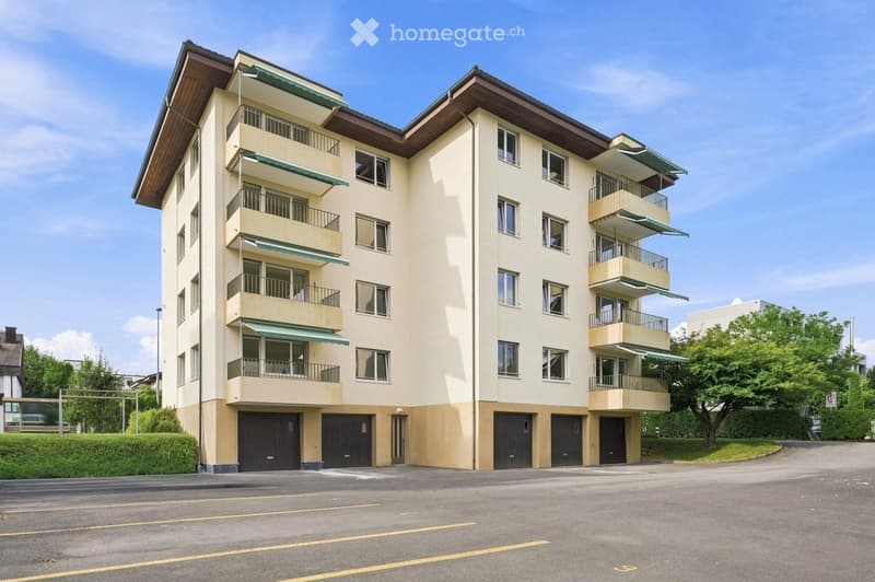 Multi-story residential building with balconies, garage, and parking area.