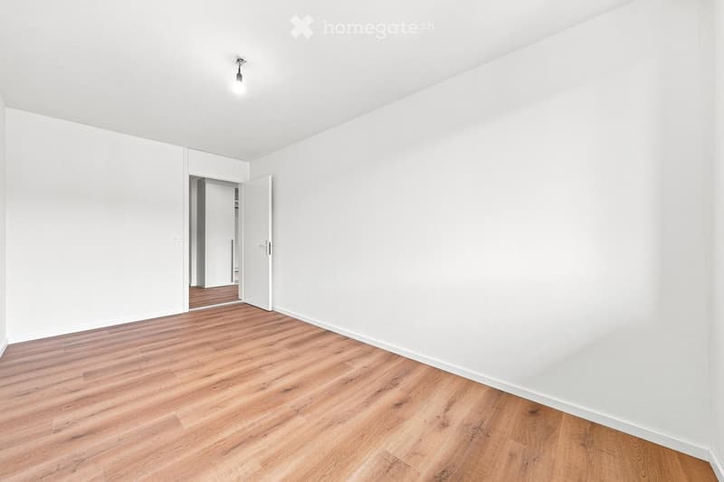 Empty room with white walls, wooden flooring, and a single open door leading to another room.
