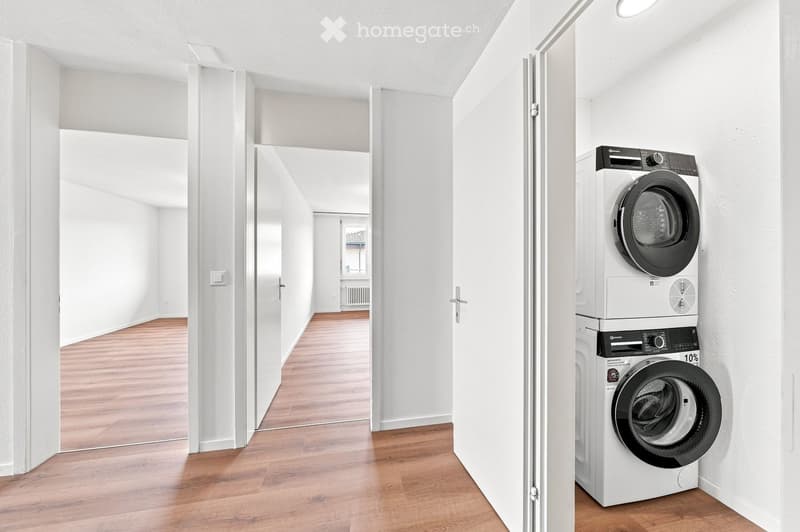 A clean, modern hallway with wooden flooring and white walls, featuring a private washing machine and dryer unit on the right side.