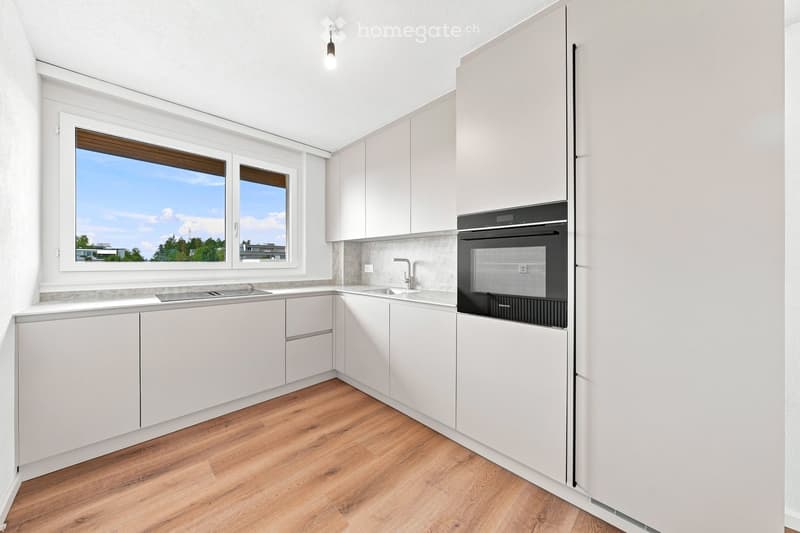 Modern kitchen with white cabinets, wooden flooring, and a large window offering a view of the outdoors.