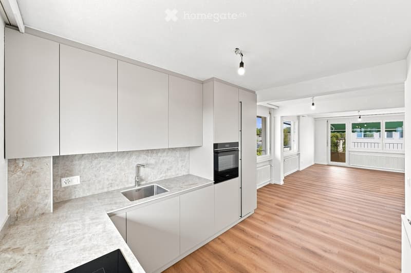 Modern kitchen with white cabinets, a stainless steel sink, and an oven. The space features a marble backsplash and light wooden flooring.