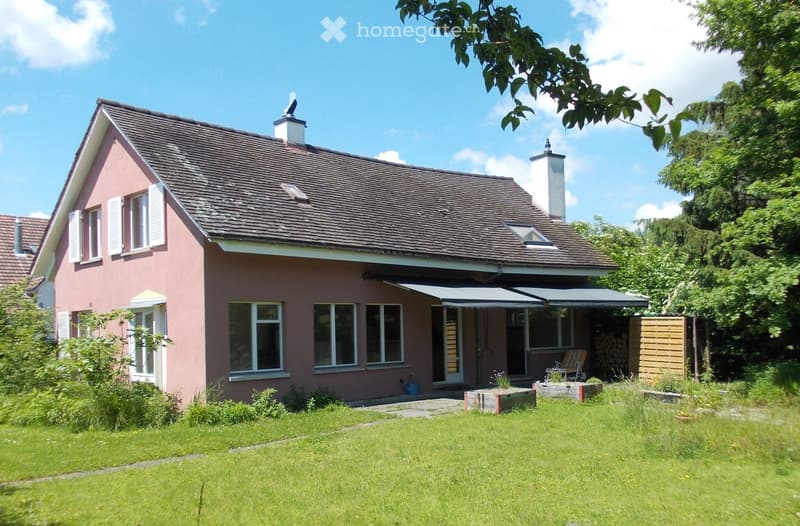 Pink single-story house with a tiled roof, multiple windows, and a covered patio area. The front yard is well-maintained with grass and small garden beds.