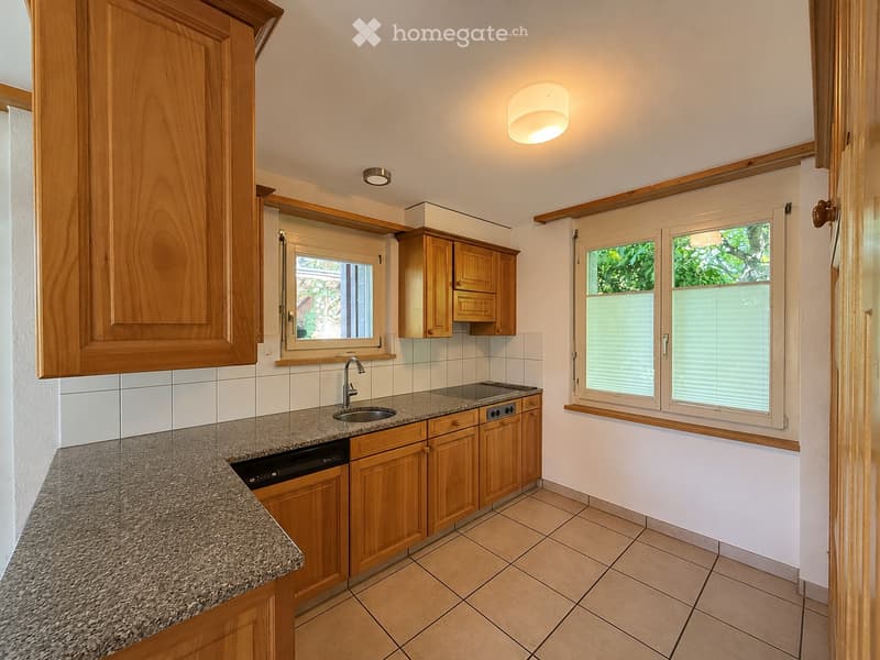 Modern kitchen with wooden cabinets, granite countertop, sink, and dishwasher. Features large windows with blinds and recessed lighting.