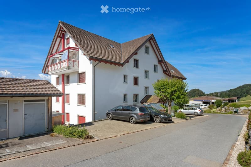 Two-story house with white walls, red trim, tiled roof, balcony, garage, and several parked cars.