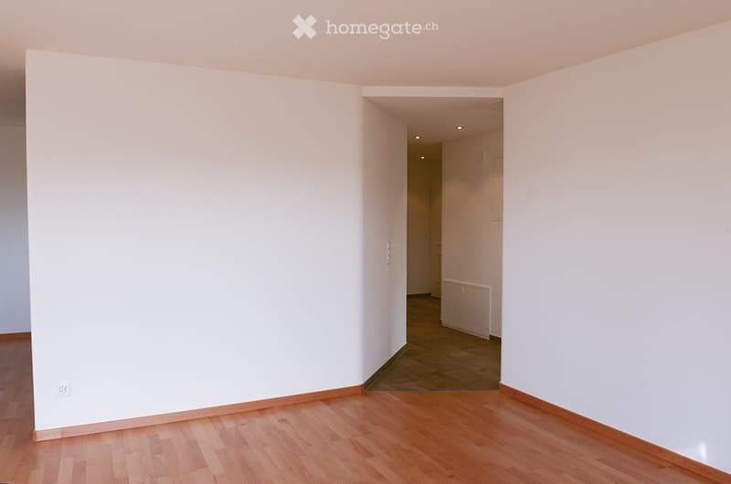 Empty room with wooden flooring and white walls, featuring a doorway leading to another room with a radiator visible.