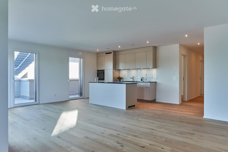 Modern kitchen with light-colored cabinets, a central island, and wooden flooring. Features include built-in appliances, ample natural light, and recessed ceiling lighting.