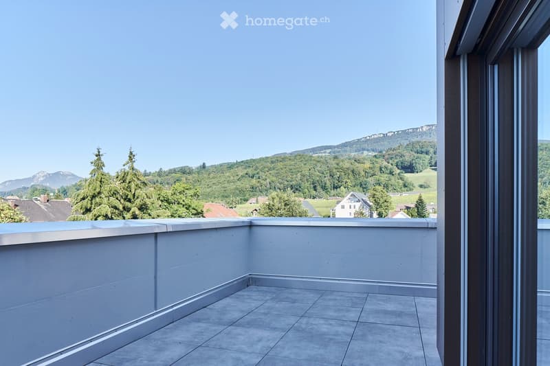 Modern balcony with tiled floor, white walls, and a panoramic view of a green landscape and mountains.