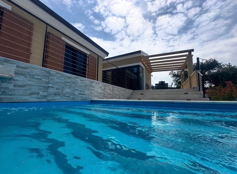 Modern outdoor area with a swimming pool, raised ground floor, patio furniture, and a wooden pergola.