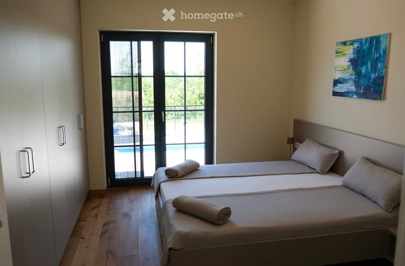 Cozy bedroom with two single beds, a large window with a view of a swimming pool, a painting on the wall, and a wardrobe.