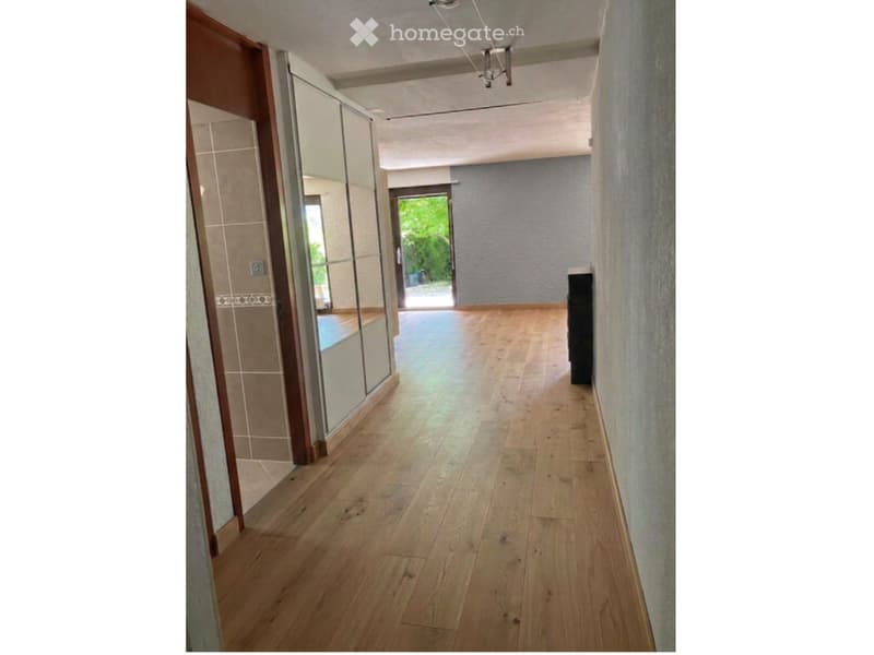 Empty hallway with wooden flooring, light-colored walls, and a glass door leading to an outdoor area.