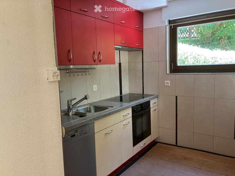 Modern kitchen with red upper cabinets, beige lower cabinets, granite countertop, sink, faucet, oven, and dishwasher. Features a window with a view of greenery outside.