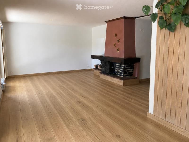 Empty room with light wooden flooring and a fireplace with a dark wooden mantel and a brick base.