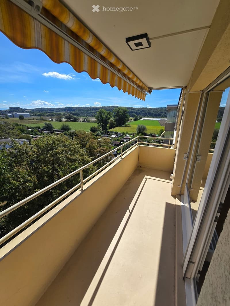 Balcony with a striped awning, metal railing, and scenic countryside view.