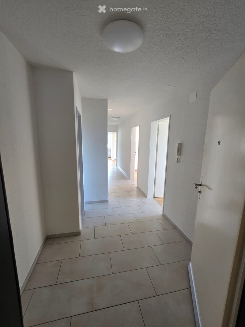 Empty hallway with tiled floor, white walls, and several doors leading to other rooms.