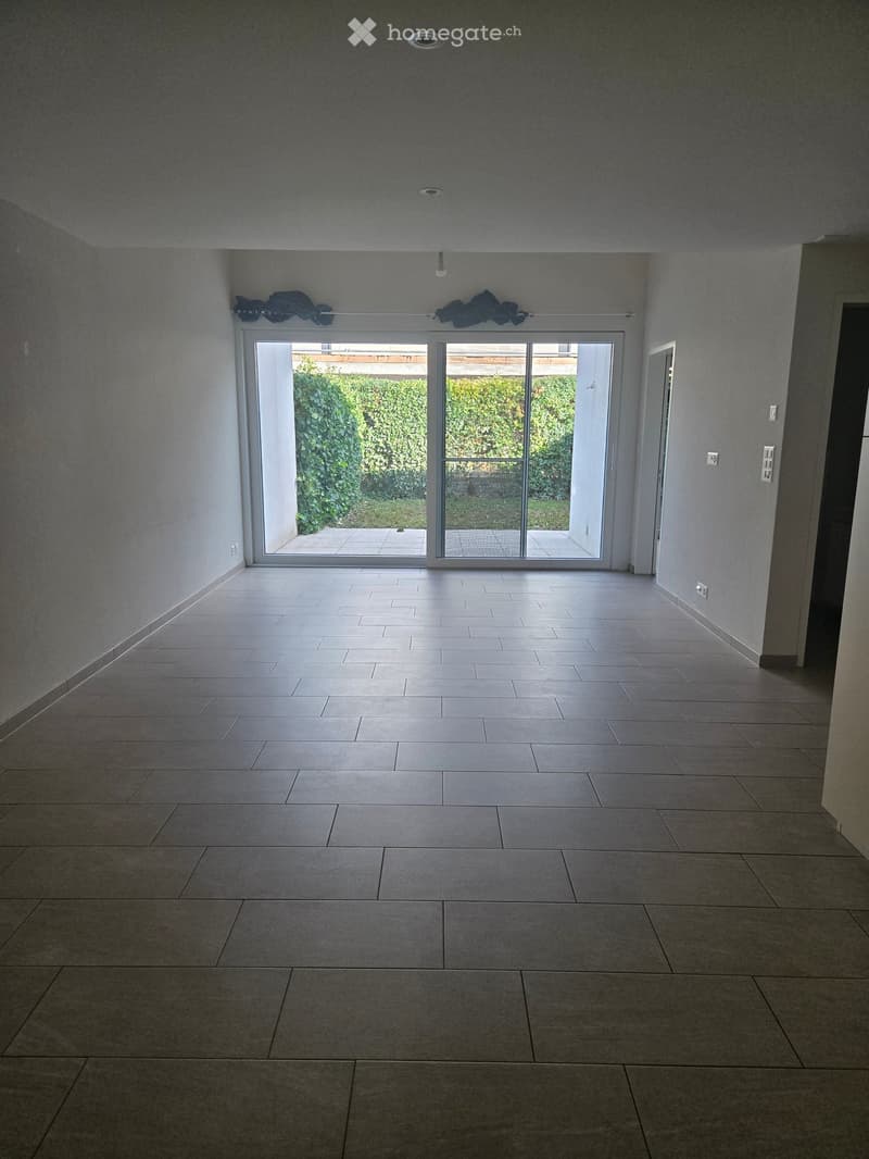 Empty room with tiled floor, large sliding glass doors leading to an outdoor area, and neutral-colored walls.