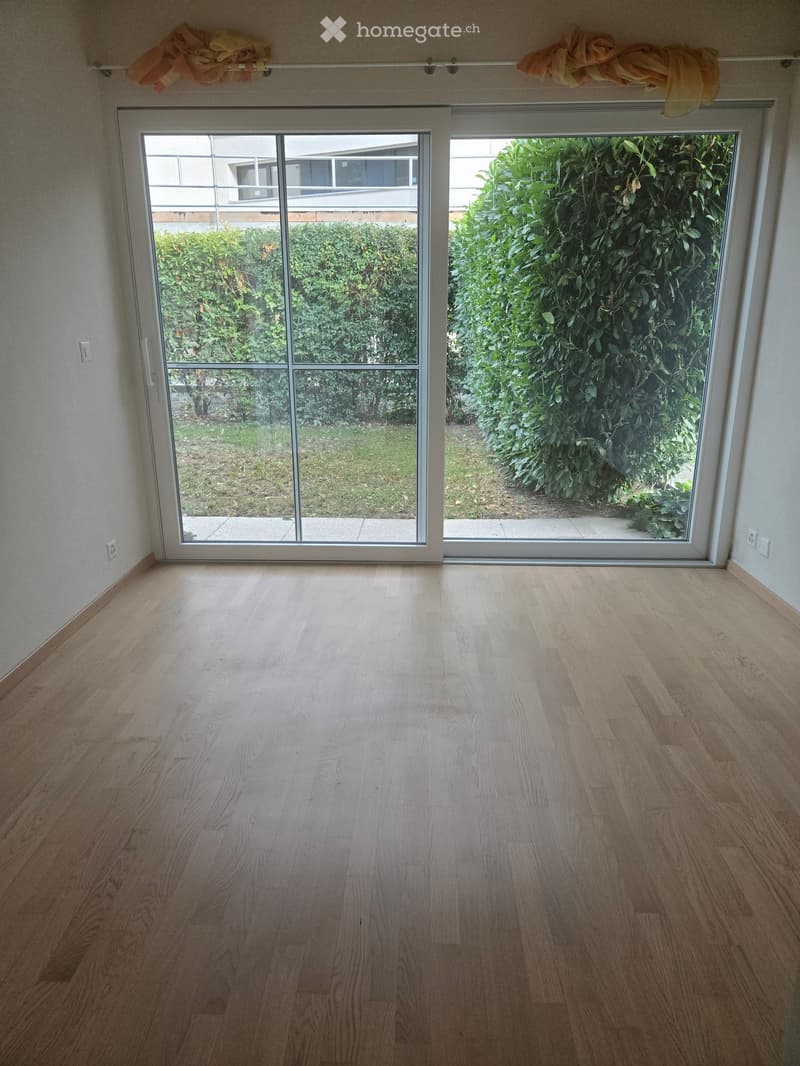 Empty room with light wooden flooring and large sliding glass doors leading to a garden area.
