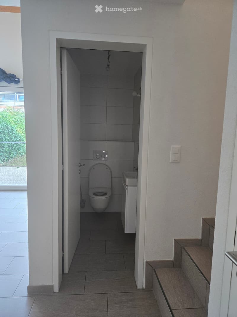 Modern bathroom with a toilet, sink, and cabinet. The space is clean and well-lit with tiled walls and floor.