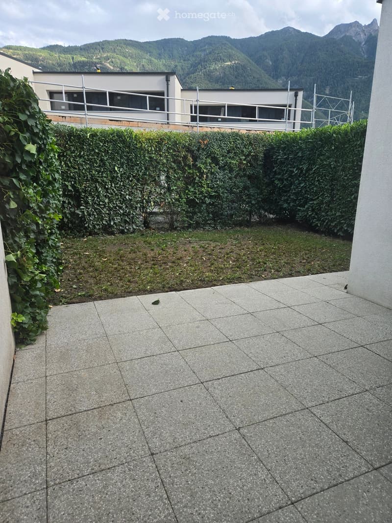 Balcony with tiled floor, metal railing, and a view of a modern building and distant mountains.