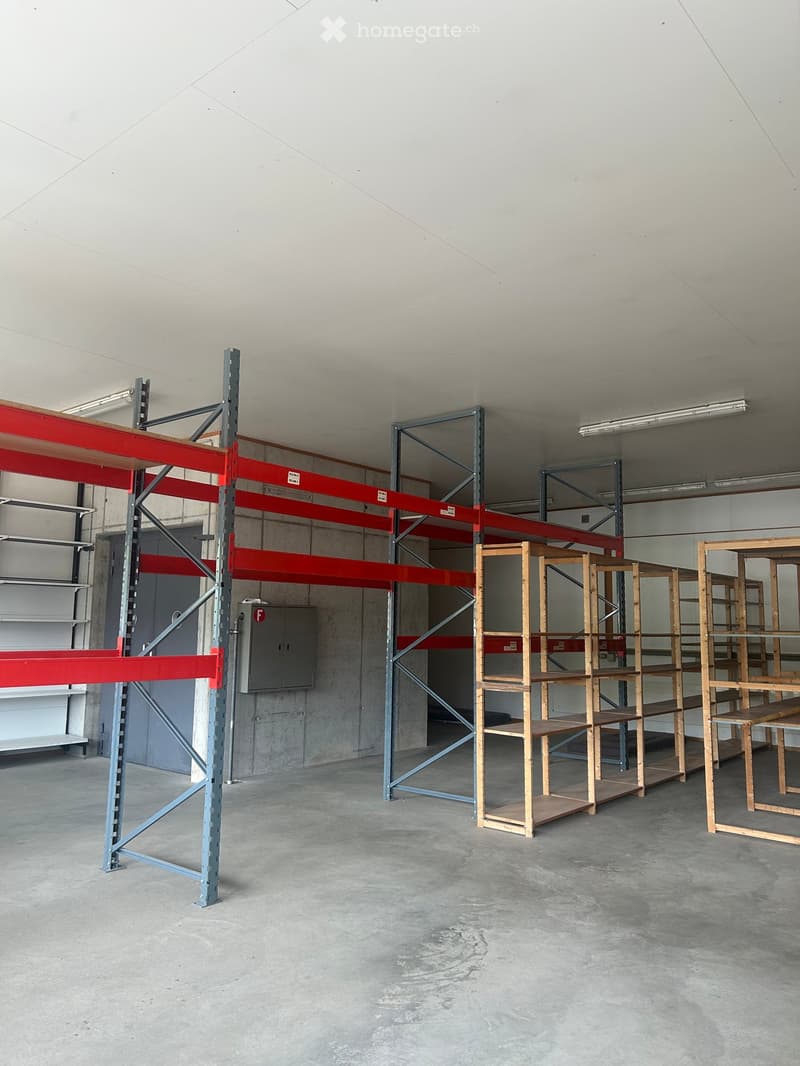 Empty warehouse space with concrete floors and walls, featuring metal shelving units and wooden shelving units.