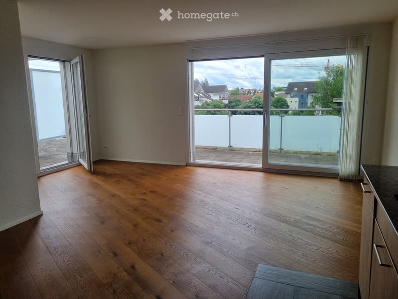 Empty room with wooden flooring, large sliding glass doors leading to a balcony, and a view of the surrounding area.