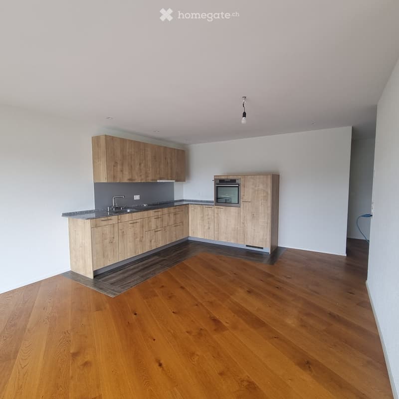 Empty kitchen with wooden cabinets, granite countertop, and wooden flooring. No appliances or furniture are present.