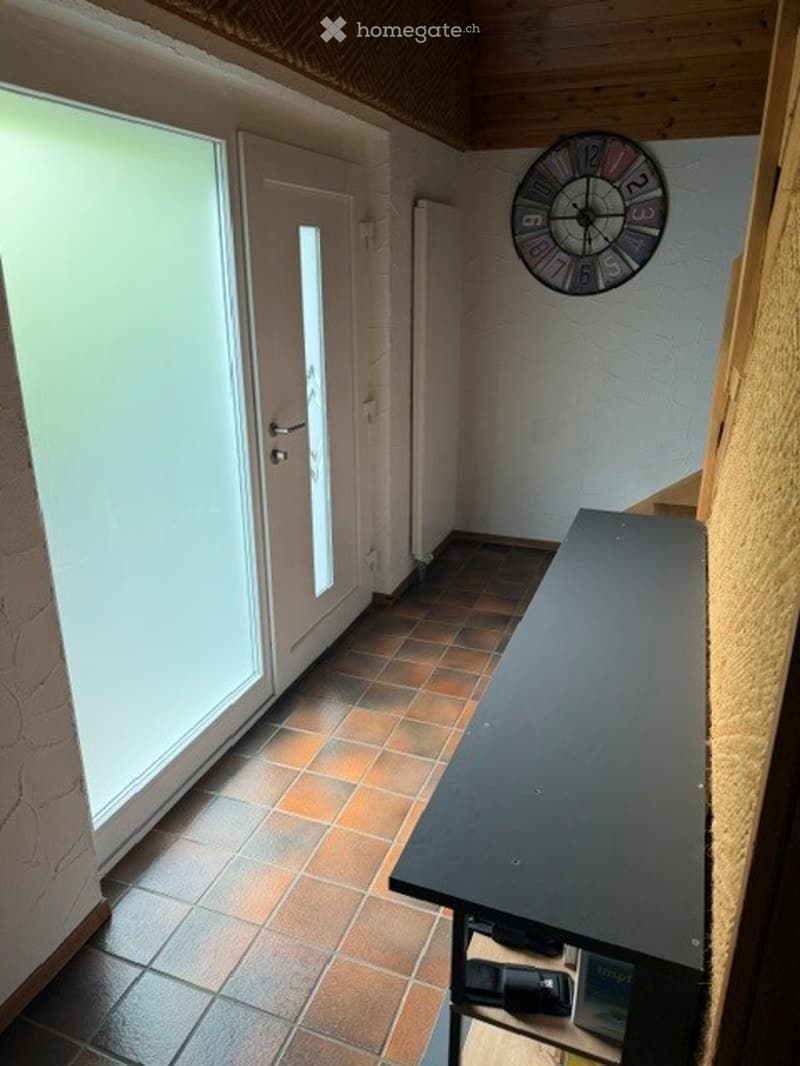Hallway with tiled floor, wooden ceiling, large window, door, and a wall-mounted clock.