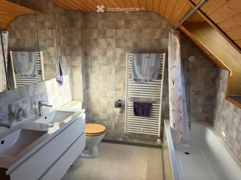 Modern bathroom with two sinks, a toilet, a bathtub, a radiator with towels, and a mirror above the sinks.