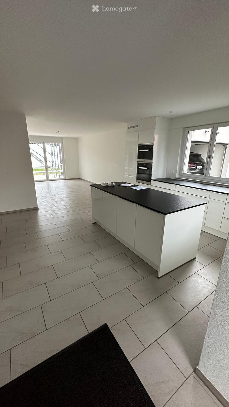 Empty kitchen with white cabinets, black countertop, tiled floor, and large windows overlooking a parking area.